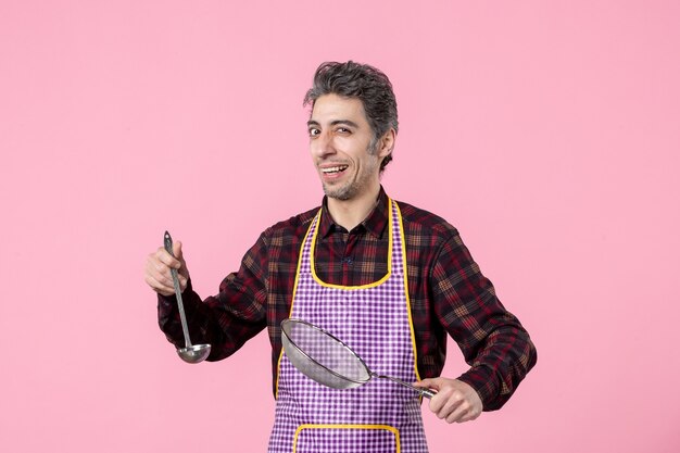 vista frontal jovem macho na capa com peneira e colher no fundo rosa trabalhador uniforme comida marido cozinheiro cozinha horizontal cozinha profissão