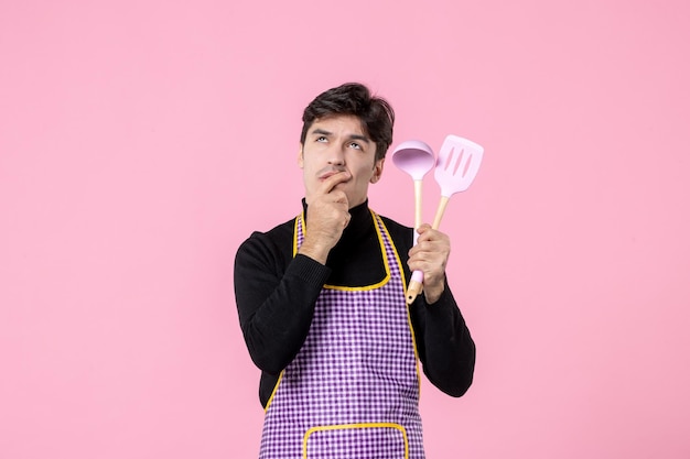 Vista frontal jovem macho na capa segurando colheres no fundo rosa profissão comida cozinhar refeição massa horizontal cozinha cor de trabalho