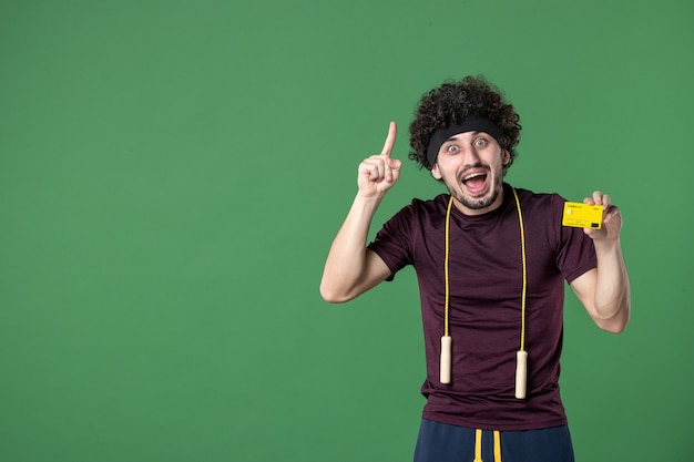 vista frontal jovem macho segurando cartão amarelo sobre fundo verde dinheiro estilo de vida treino esporte atleta saúde ginásio