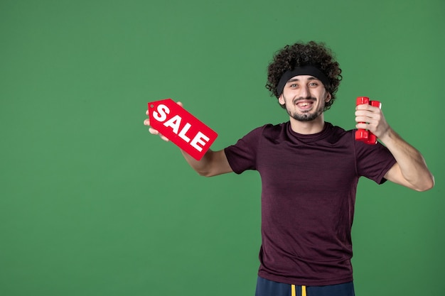 vista frontal jovem macho segurando halteres e venda escrevendo sobre fundo verde esporte ginásio cor treino saúde atleta compras