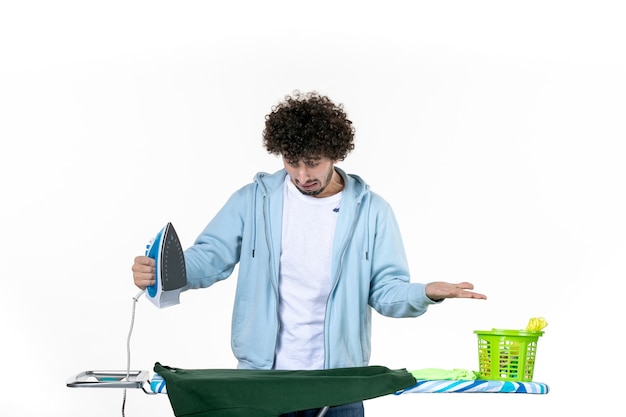 vista frontal jovem masculino passando camisa verde e queimando-a acidentalmente no fundo branco trabalho doméstico cor ferro humano lavanderia lavagem a seco roupas