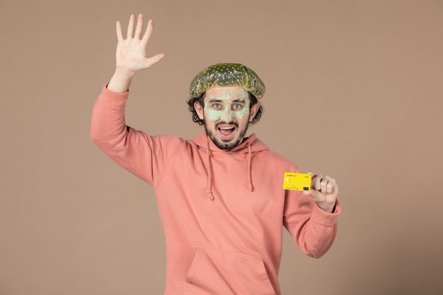 vista frontal jovem masculino segurando um cartão de crédito amarelo sobre fundo marrom pele salão terapia skincare facial bodycare spa dinheiro