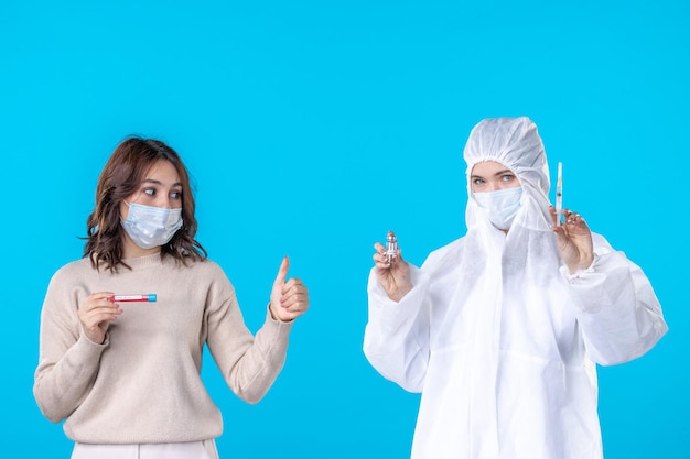 vista frontal jovem médica em traje de proteção com paciente em fundo azul ciência doença vírus médico covid- isolamento pandêmico