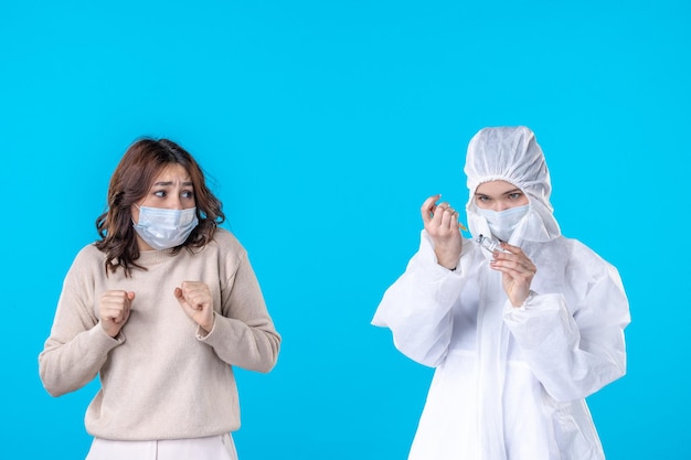 Foto vista frontal jovem médica em traje de proteção com paciente sobre o fundo azul ciência doença covid- pandemia saúde isolamento vírus médico