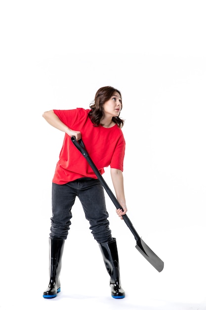 Vista frontal jovem mulher de camisa vermelha imitando cavar com pá preta sobre fundo branco cor do solo trabalho mulher emoção cemitério trabalho de solo