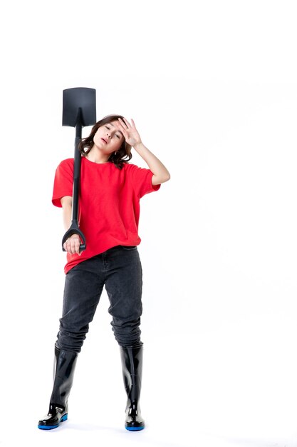 vista frontal jovem mulher de camisa vermelha, segurando uma pá preta, sentindo-se cansada no fundo branco solo trabalho mulher solo trabalho natureza emoção cemitério