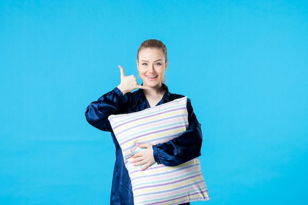 vista frontal jovem mulher de pijama segurando travesseiro na cor de fundo azul sono pesadelo festa sonho cansado descanso cama mulher bocejar