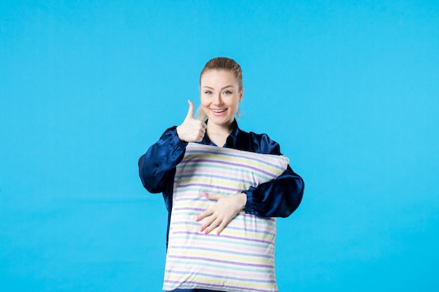 vista frontal jovem mulher de pijama segurando travesseiro sobre fundo azul cor da mulher cama noite sonho pesadelo descanso bocejo sono