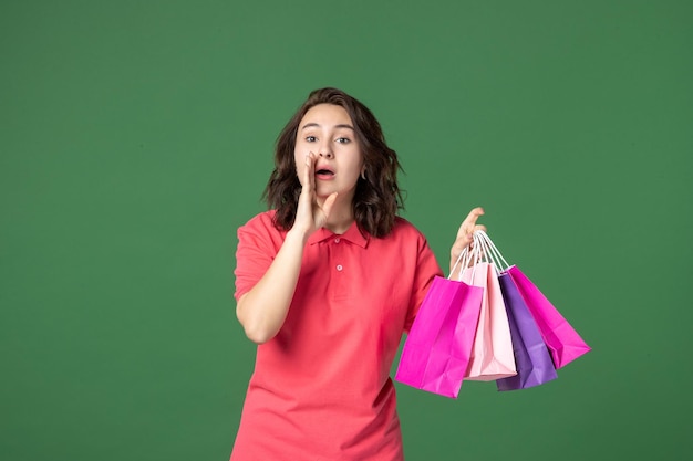 Vista frontal jovem vendedora segurando pacotes e sussurrando sobre fundo verde trabalho cor trabalhador boutique venda presente uniforme de compras