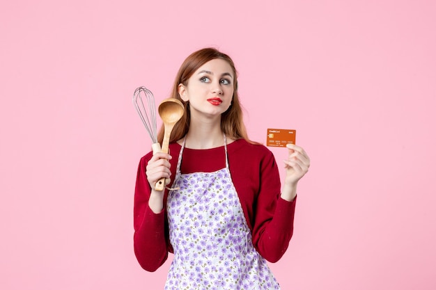 Vista frontal joven ama de casa sosteniendo un batidor y una tarjeta bancaria sobre fondo rosa pastel de cocina pastel mujer color compras cocinando dinero cocina