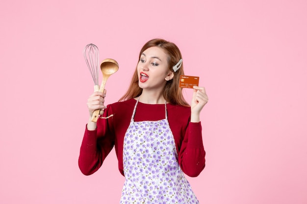Vista frontal joven ama de casa sosteniendo un batidor y una tarjeta bancaria sobre fondo rosa pastel de color cocina dulce cocina mujer pastel comida
