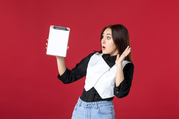 Vista frontal joven bonita camarera en uniforme sosteniendo nota de archivo para pedidos sobre fondo rojo mujer de belleza cena trabajo trabajo trabajador comida