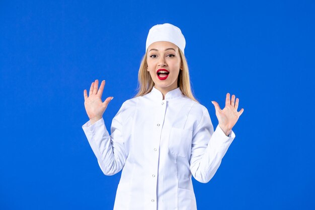 Vista frontal de la joven bonita enfermera en traje médico en la pared azul