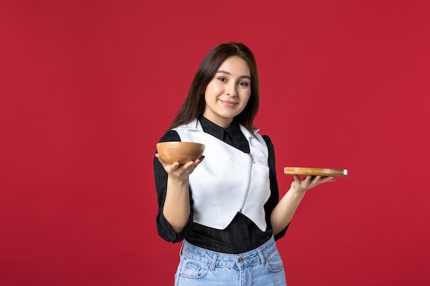 Vista frontal joven camarera sosteniendo pedidos de comida sobre fondo rojo trabajo comida trabajo comida belleza trabajador noche color cena uniforme