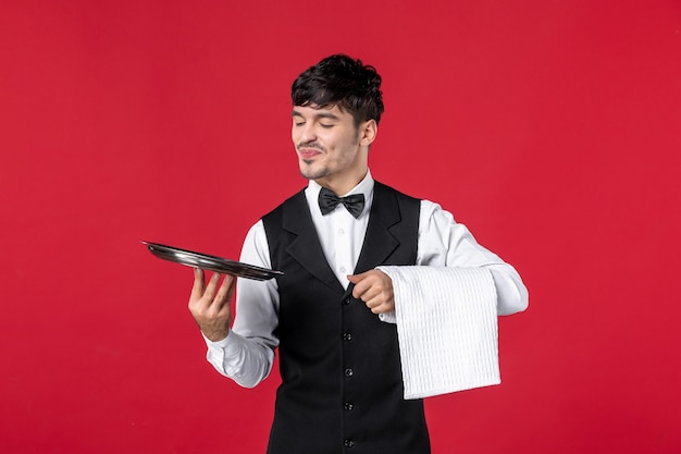 Vista frontal del joven camarero masculino feliz en un uniforme con lazo de corbata
