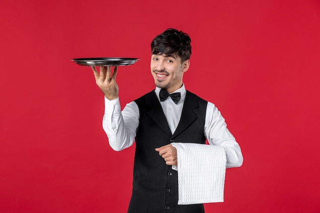 Vista frontal del joven camarero masculino sonriente en un uniforme con lazo de corbata