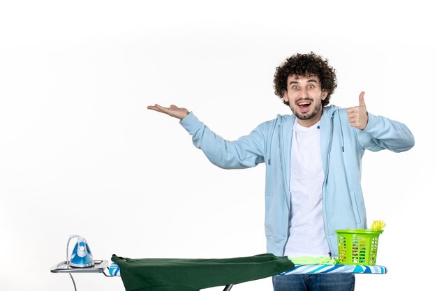 Vista frontal joven detrás de la tabla de planchar sobre fondo blanco quehaceres domésticos planchado de ropa limpieza emoción hombre color