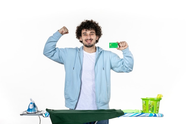 Vista frontal joven detrás de la tabla de planchar con tarjeta bancaria sobre fondo blanco lavandería quehaceres domésticos color humano limpieza dinero emoción