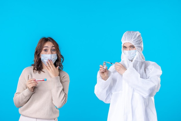 Vista frontal joven doctora en traje de protección con el paciente en el fondo azul ciencia enfermedad médica covid-pandemia virus de aislamiento de salud