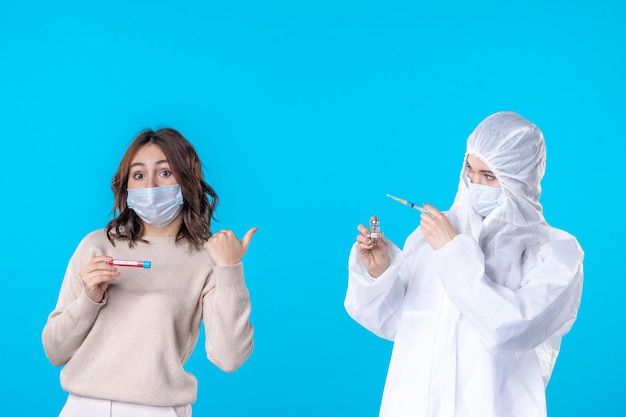 Vista frontal joven doctora en traje de protección con el paciente en el fondo azul ciencia enfermedad médica covid-pandemia virus de aislamiento de salud