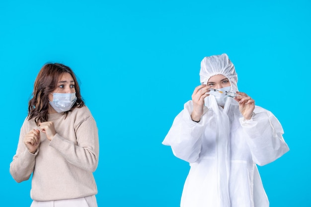 Vista frontal joven doctora en traje de protección con el paciente sobre fondo azul ciencia enfermedad covid- virus de salud pandémica médica