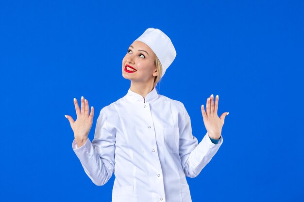 Vista frontal de la joven enfermera en traje médico blanco sobre pared azul
