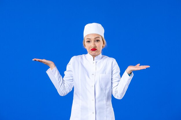 Vista frontal de la joven enfermera en traje médico blanco sobre pared azul