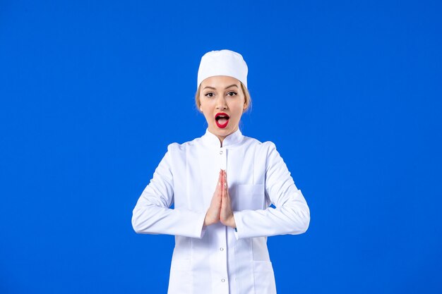 Vista frontal de la joven enfermera en traje médico blanco sobre pared azul