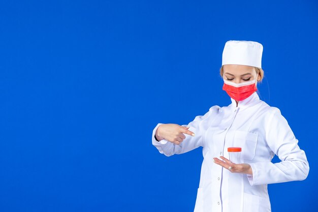 Vista frontal joven enfermera en traje médico con máscara sosteniendo matraz sobre fondo azul virus hospitalario covid- médico salud medicamentos medicamentos vacuna pandémica