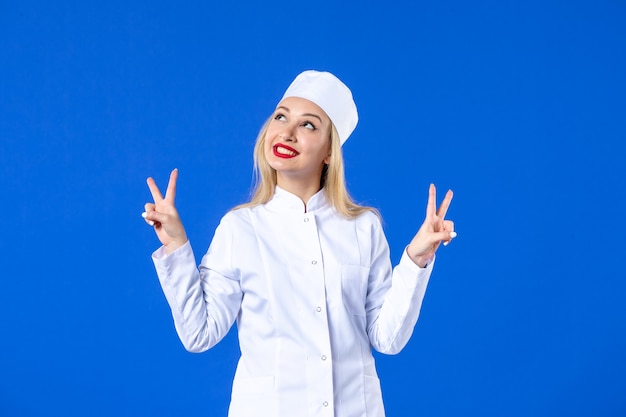 Vista frontal de la joven enfermera en traje médico en la pared azul