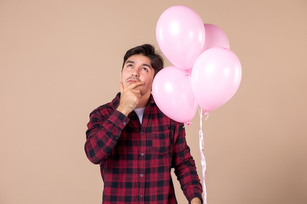 Vista frontal joven con globos de color rosa en la pared marrón