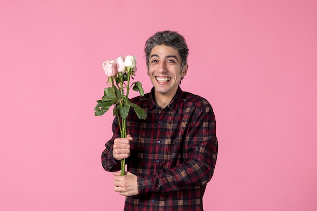 Vista frontal joven con hermosas rosas rosadas sonriendo en pared rosa