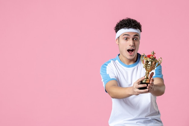 Vista frontal del joven jugador de béisbol en ropa deportiva con copa de oro