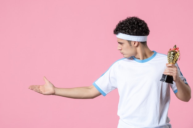 Foto vista frontal joven jugador en ropa deportiva con copa de oro en pared rosa