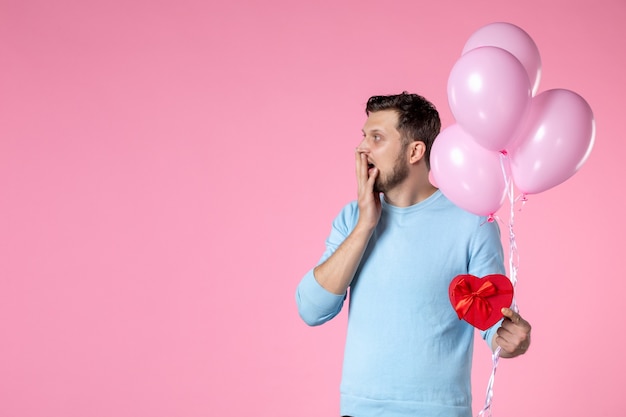 Vista frontal joven con lindos globos rosados y presente en forma de corazón sobre fondo rosa igualdad sensual día de la mujer marcha de matrimonio amor parque fecha diversión