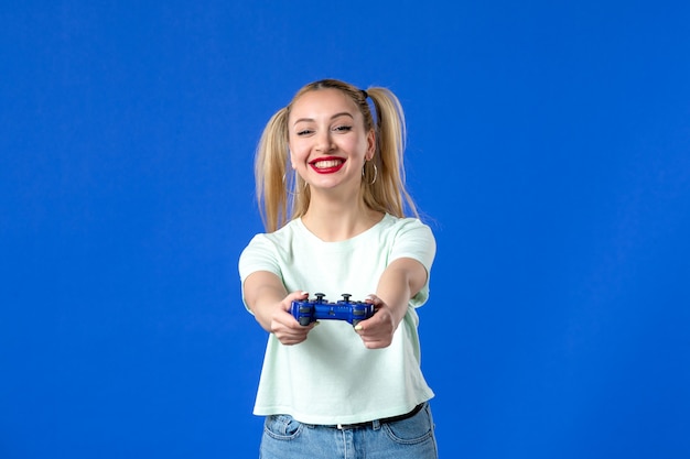 Vista frontal joven mujer con gamepad sobre fondo azul alegre jugador juvenil virtual adulto ganando video sofá de internet