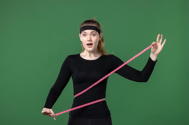 Vista frontal joven mujer midiendo su cuerpo con centímetro en verde