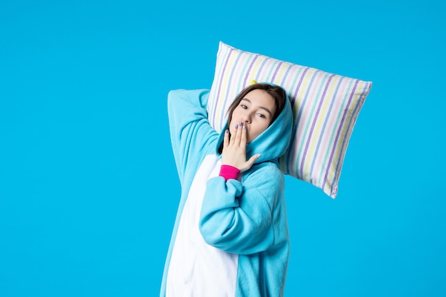 Vista frontal joven mujer en pijama para fiesta de pijamas sosteniendo almohada sobre fondo azul cama mujer descansar tarde divertidos sueños juego dormir pesadilla noche