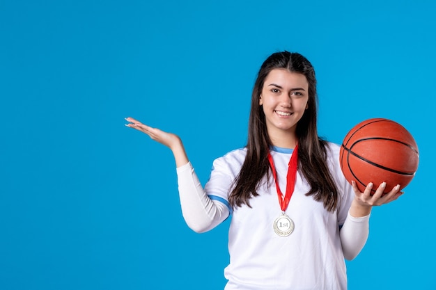 Vista frontal joven mujer sosteniendo baloncesto en pared azul