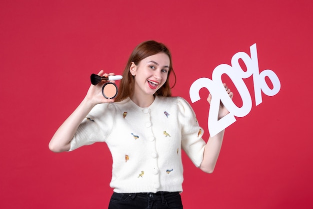 Vista frontal joven mujer sosteniendo borla maquillaje en polvo y escribiendo sobre fondo rojo igualdad sensual día de la mujer marzo matrimonio compras moda colores