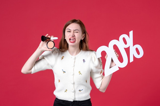 Vista frontal joven mujer sosteniendo borla maquillaje en polvo y escribiendo sobre fondo rojo piel mujer marcha compras cuidado de la piel moda sensual labios de color