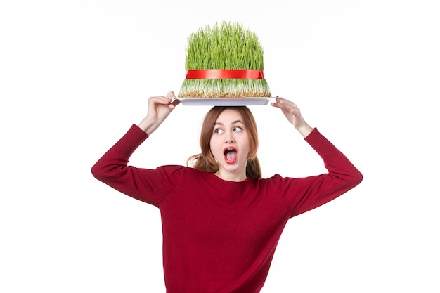 Vista frontal joven mujer sosteniendo gran verde novruz semeni en su cabeza sobre fondo blanco primavera étnico ejecutante concepto colores vacaciones familia