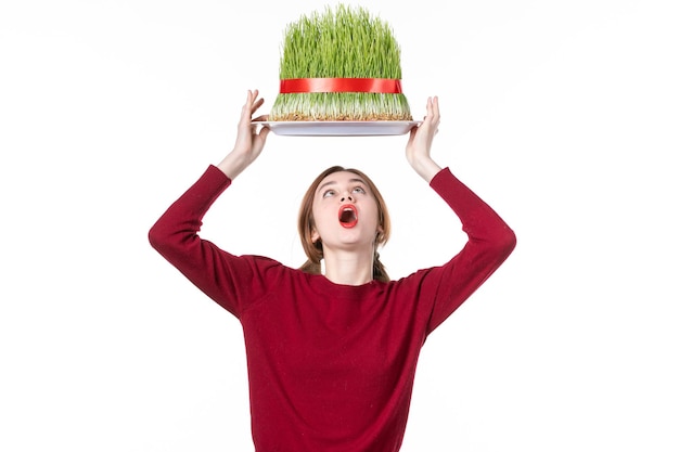 Vista frontal joven mujer sosteniendo gran verde novruz semeni en su cabeza sobre fondo blanco primavera étnico ejecutante etnicidad concepto colores vacaciones