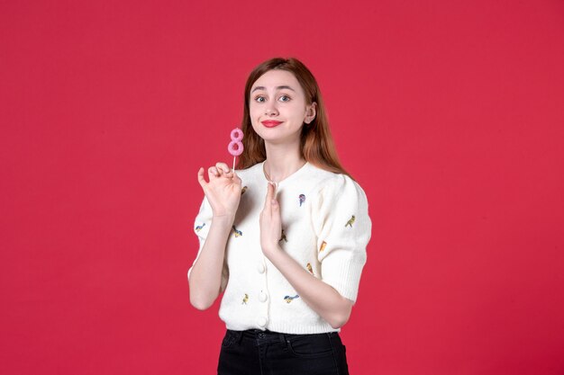 Vista frontal joven mujer sosteniendo pegatina rosa sobre fondo rojo amor sensual compras matrimonio día de la mujer marzo igualdad