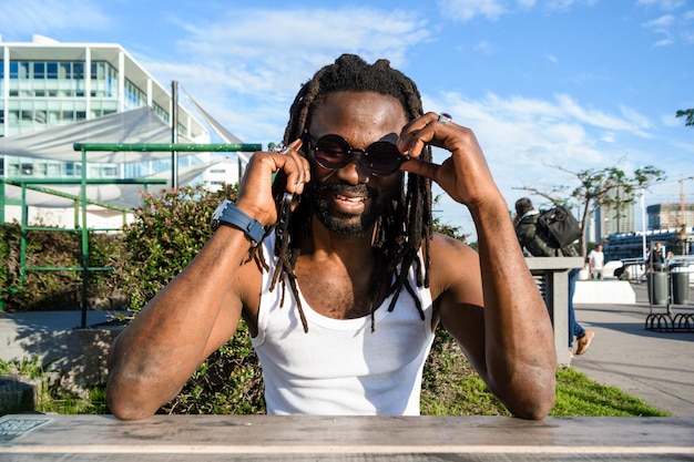 Vista frontal de un joven negro feliz con dreadlocks sentado hablando por teléfono