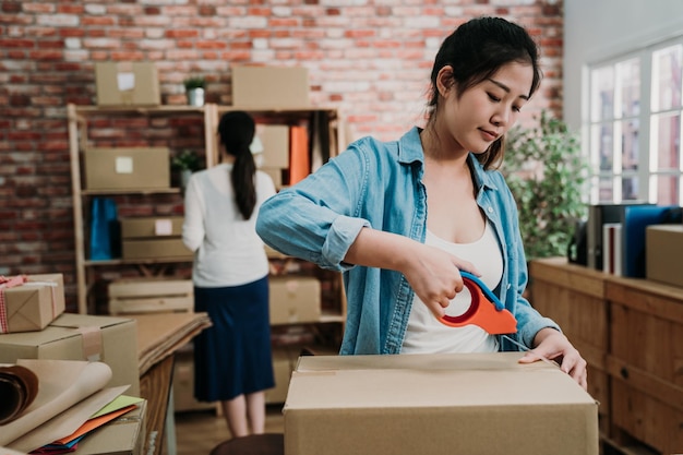 vista frontal de la joven propietaria de una pequeña empresa empacando cartón en el lugar de trabajo usando cinta adhesiva. una vendedora emprendedora independiente prepara una caja de paquetes para entregar el producto al cliente. vender en línea