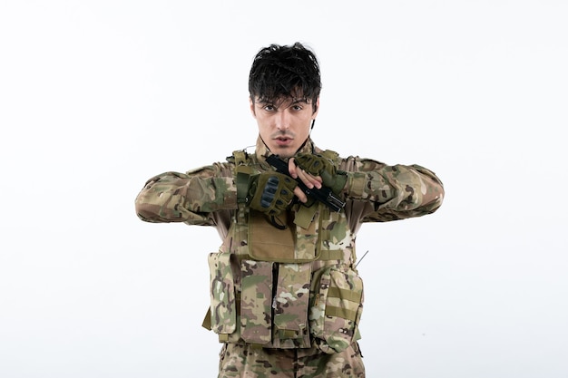 Vista frontal del joven soldado en camuflaje con pistola pared blanca