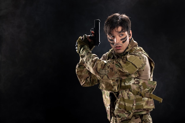 Vista frontal del joven soldado de camuflaje con pistola en pared negra