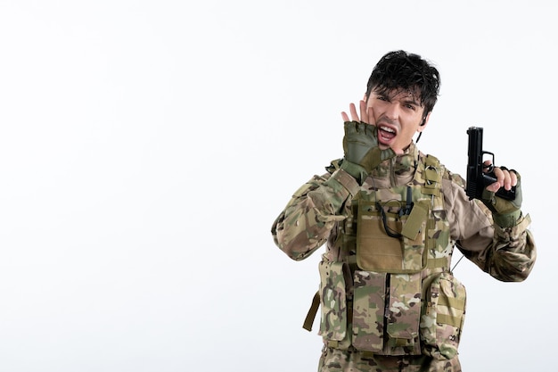 Vista frontal joven soldado en uniforme militar con pistola pared blanca