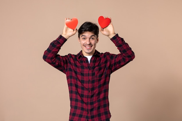 Vista frontal joven sosteniendo pegatinas de corazón rojo en la pared marrón